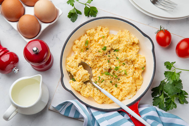scrambled eggs for breakfast on frying pan, white table, top view - Foto, afbeelding