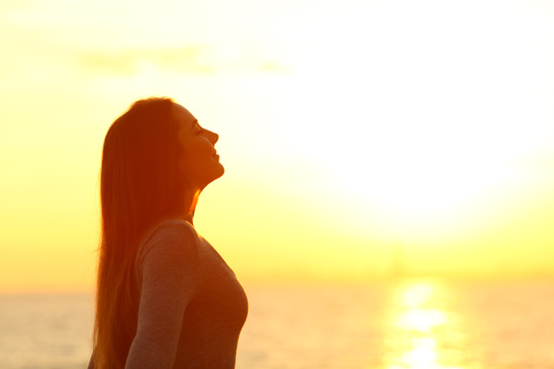 Zijaanzicht portret van een ontspannen vrouw ademt diep frisse lucht bij zonsondergang op het strand - Foto, afbeelding