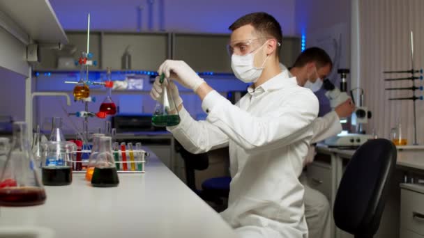 Jonge wetenschapper mengen gekleurde vloeistoffen - Video