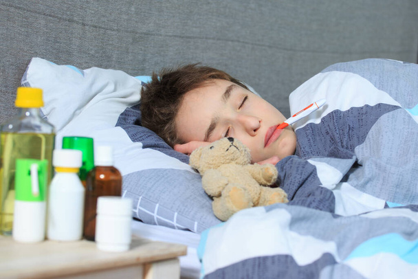 病気の少年が口の中に体温計を持ってベッドに横になり - 写真・画像