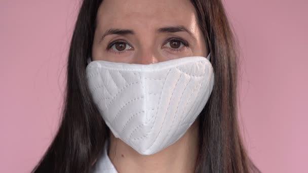 Young woman wearing a protective face mask during the Coronavirus disease (COVID-19) outbreak epidemic. Close up portrait with a multiple use white protection mask on the face shot in a studio. - Footage, Video
