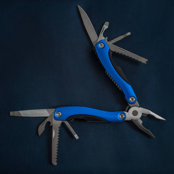 A beautiful folding knife, a mobile male tool and an accessory with several tools for work and repair on a dark blue background. - Fotografie, Obrázek