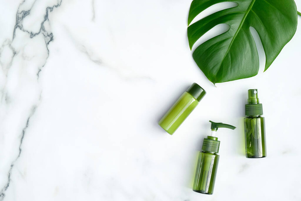 SPA cosmetic bottles and green tropical leaf on marble background. Natural organic beauty products for skincare, body and hair care. Flat lay, top view, copy space - Valokuva, kuva
