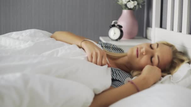 Γυναίκα ξυπνάει και τεντώνεται σε λευκό κρεβάτι στην κρεβατοκάμαρα - Πλάνα, βίντεο