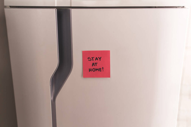 Nota pegajosa en el refrigerador diciendo Quédese en casa
! - Foto, Imagen