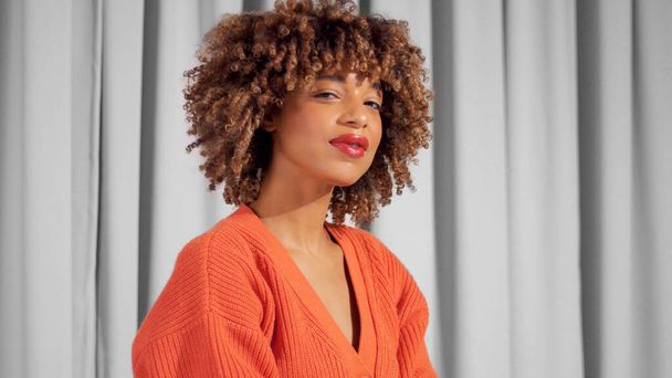 ミックスレース黒大人女性肖像上のグレーカーテンで明るいオレンジニットジャケット - 写真・画像