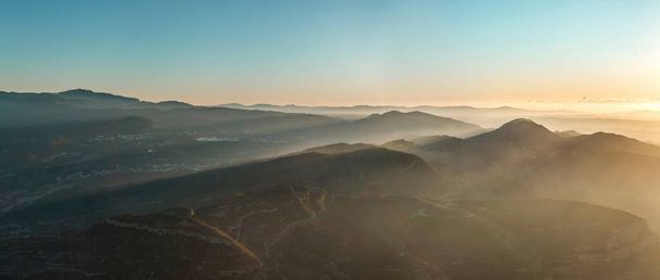 Amanecer en una zona montañosa donde la niebla destaca los rayos del sol entre las montañas.. - Foto, Imagen