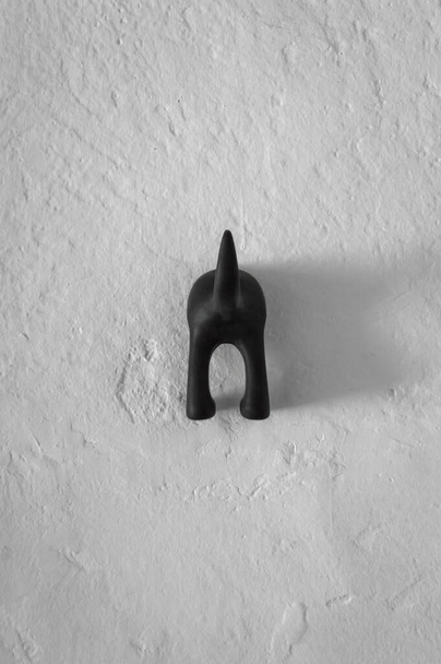 Забавна вішалка або кілок з формою собачої дупи на пошкодженій білій стіні. Прекрасна і приваблива прикраса у вертикальному погляді
. - Фото, зображення