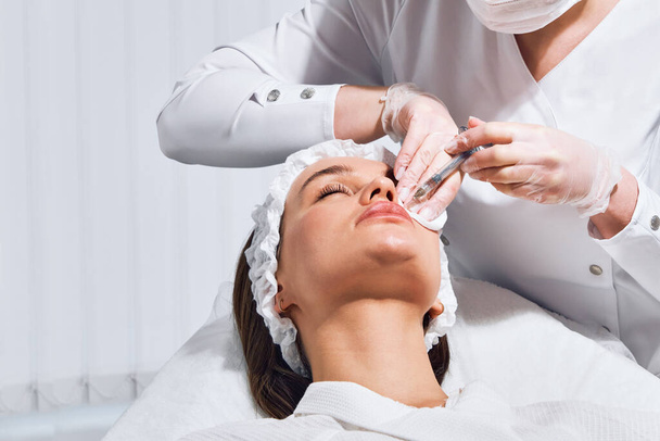 lip vorm correctie procedure in een cosmetologie salon. De specialist geeft een injectie op de lippen van de patiënt. Lipvergroting - Foto, afbeelding