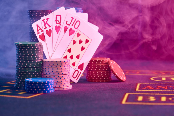 Winnende combinatie in poker staan leunen op veelkleurige chips stapels op een blauwe cover van een speeltafel. Zwart, rookachtergrond met rode en blauwe achtergrondverlichting. Gokken entertainment, speelkaarten, casino concept. Close-up opname. - Foto, afbeelding