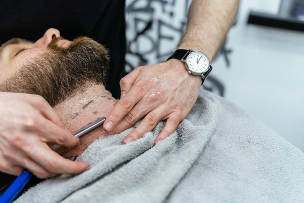 Scheerproces van baarden in Barbershop. close-up shot van kapper maakt een kapsel baard client met rechte scheermes. - Foto, afbeelding