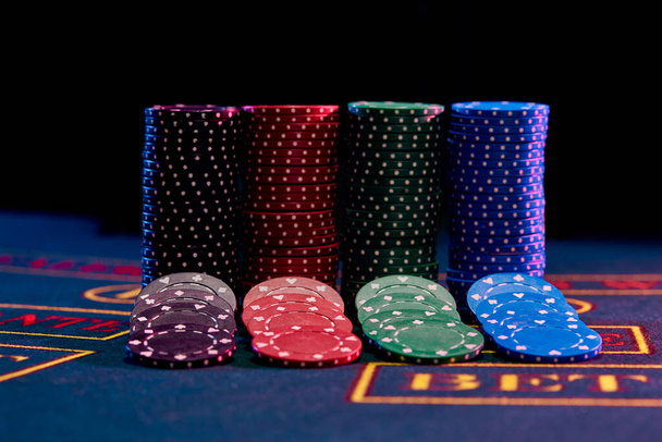 Barevné žetony jsou pěkně rozložené u hromady stojící na modrém obalu hracího stolu se značkou. Černé pozadí. Hazardní hry, poker, kasino koncept. Detailní záběr. - Fotografie, Obrázek
