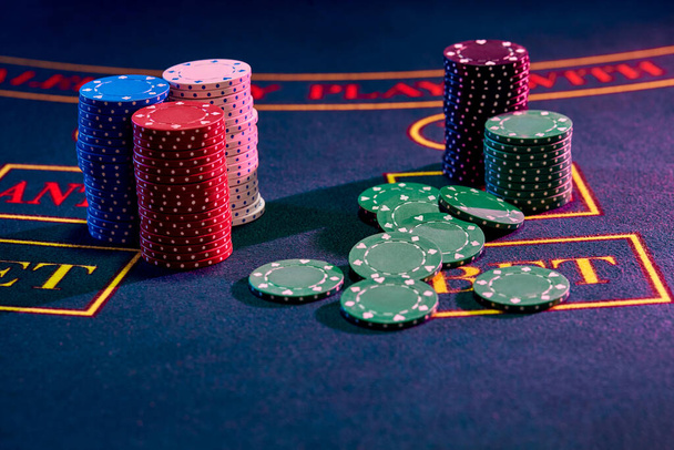 Multicolored chips piles, some green ones are laying nearby on a blue cover of a playing table with markup. Gambling entertainment, poker, casino concept. Close-up shot. - Photo, Image