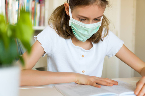 Karantina sırasında ders kitabı okuyan küçük bir kız. Coronavirus konsepti. - Fotoğraf, Görsel