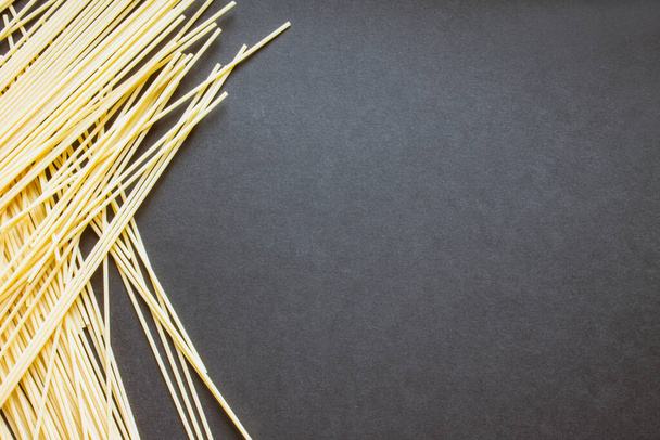 Raw spaghetti scattered on a black background with copy space - Photo, image