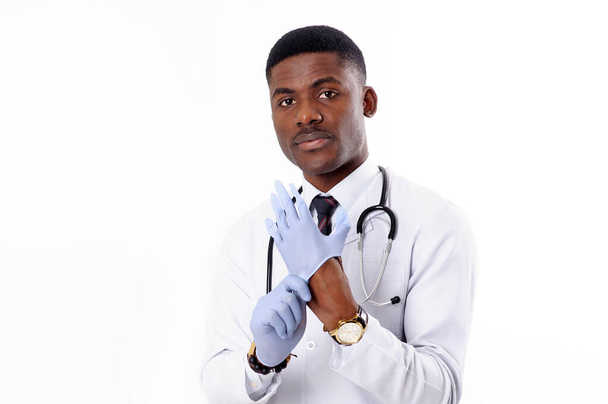 Young african handsome doctor on white isolated background with phonendoscope puts on medical gloves - Foto, immagini