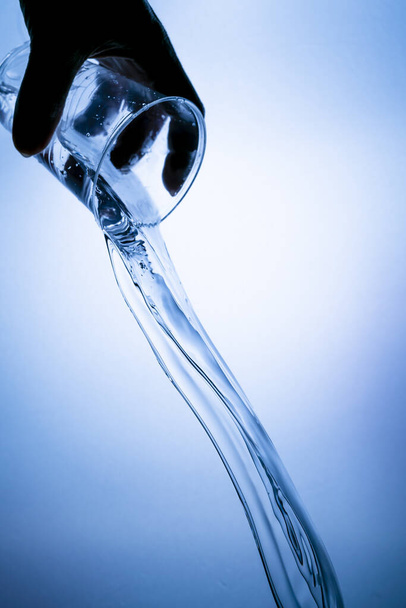 Ruka drží plastovou sklenici s vodou stříkající na modrém pozadí - Fotografie, Obrázek
