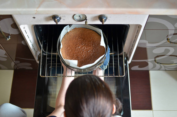 Vrouw handen nemen van kant-en-klare taart uit de oven.  - Foto, afbeelding