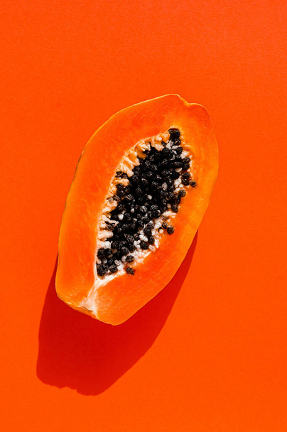 Fresh papaya exotic tropical fruit on orange background. Sun day light illumination. Minimalistic summer flat lay wallpaper. Creative food concept. Copy space template. Bold colors - 写真・画像