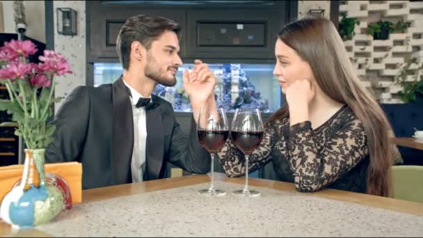 Молодий чоловік цілує руку красивої жінки, на столі два келихи вина. На підлозі є сноуборд
. - Кадри, відео