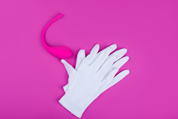 Vibrador rosa (consolador) para la comodidad de las mujeres sobre un fondo rosa con guantes blancos
. - Foto, imagen