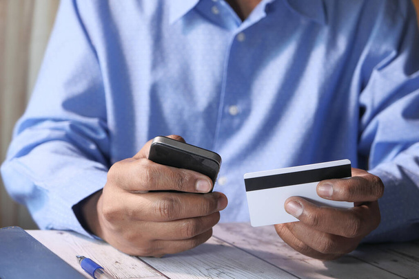 Mans mãos segurando um cartão de crédito usando telefone inteligente para compras on-line
 - Foto, Imagem