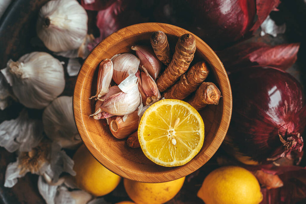 Bowl with turmeric, garlic, lemon with garlic, lemon and onion in the background - Fotó, kép