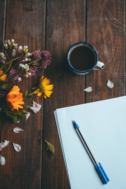 Papier und Stift mit Frühlingsblumen und einer kleinen weißen Tasse Kaffee auf einem rustikalen Holztisch - Foto, Bild