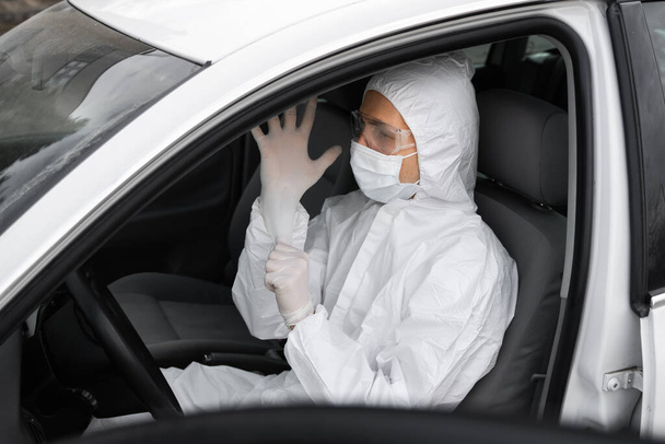 Man in protective suit, medical mask and rubber gloves for protect from bacteria and virus is planning to drive. Protective mask while quarantine, world pandemic, covid 19, coronavirus, infection. - Foto, immagini