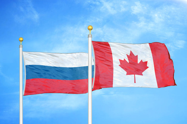 Rosja i Kanada dwie flagi na maszcie flagowym i niebieskie zachmurzone tło nieba - Zdjęcie, obraz