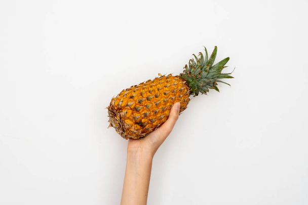 Female hand holding ripe pineapple on a white background. - Foto, Imagen