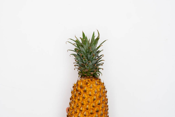 Female hand holding ripe pineapple on a white background. - Foto, afbeelding