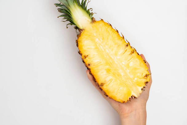 Female hand holding a half of ripe pineapple on a white background. - Foto, imagen