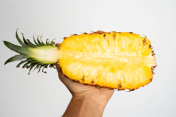 Female hand holding a half of ripe pineapple on a white background. - Photo, Image