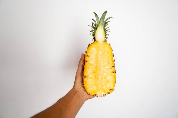 Female hand holding a half of ripe pineapple on a white background. - Фото, изображение