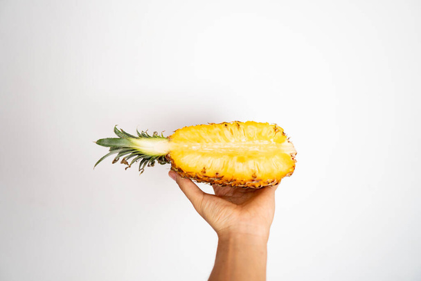 Female hand holding a half of ripe pineapple on a white background. - Foto, Imagem
