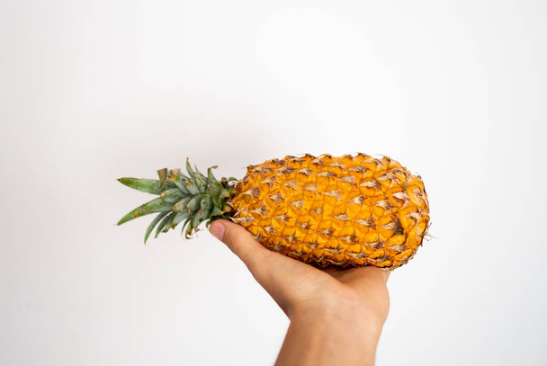Female hand holding ripe pineapple on a white background. - Фото, изображение