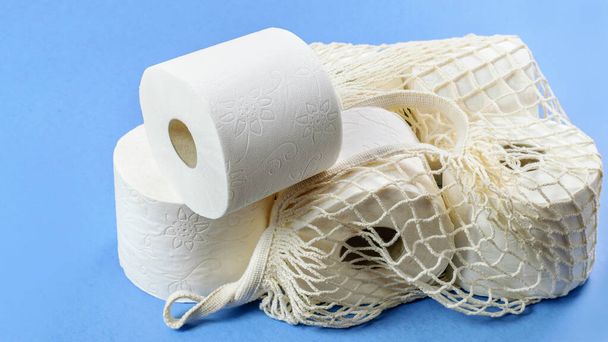 Toilettenpapier in Rollen in der weißen Tasche auf blauem Hintergrund Nahaufnahme. Täglich hygienisches Produkt. Gesunde Sauberkeit.  - Foto, Bild
