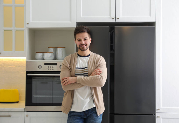 Happy young man near refrigerator in kitchen - Foto, Bild