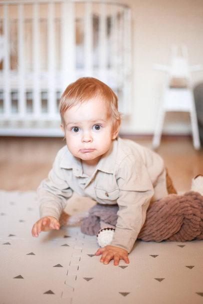 egy egyéves fiú bézs ingben, és a padlón ül a szobájában. - Fotó, kép
