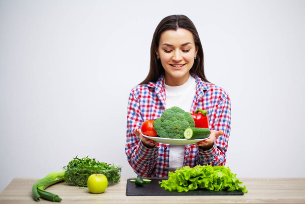 Le concept de manger sainement et la jeune fille alimentation tenant des légumes sur le fond mur blanc
 - Photo, image