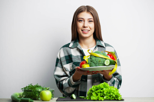 Het concept van gezond eten en dieet meisje met groenten op de achtergrond witte muur - Foto, afbeelding