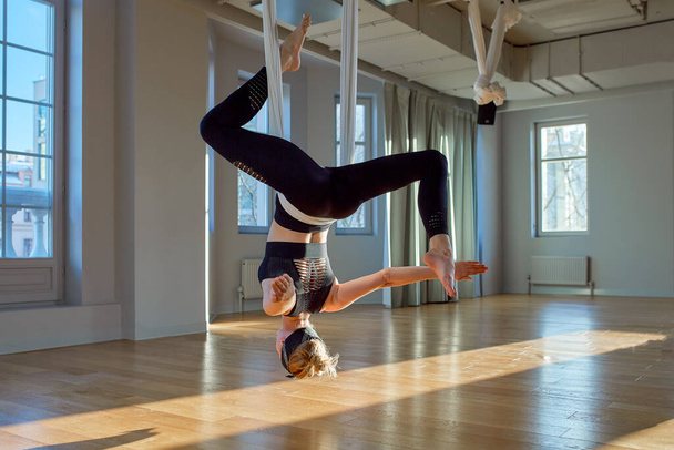 Beautiful girl aerial yoga trainer shows medutiruet on hanging lines upside down in a yoga room. Concept yoga, flexible body, healthy lifestyle, fitness. - Valokuva, kuva