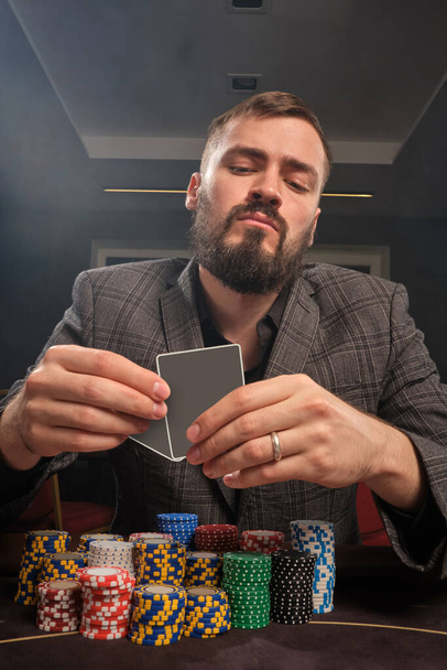 Baard man in een klassiek pak, met veel chips is het spelen van poker zitten aan de tafel in het casino. Hij gokt op een grote overwinning. Gokken voor geld. Spelen van het geluk. - Foto, afbeelding
