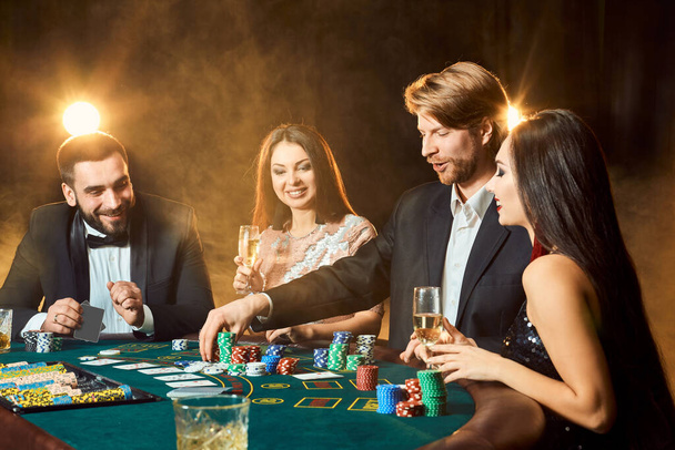 Des amis de la classe supérieure jouant dans un casino. Deux hommes en costume et deux jeunes femmes en robe. Fumée. Casino. Poker
 - Photo, image