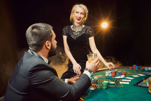 Группа молодых богатых людей играет в покер в казино. Мужчина в деловом костюме и две молодые женщины в черных платьях. Дым. Казино. Покер
 - Фото, изображение