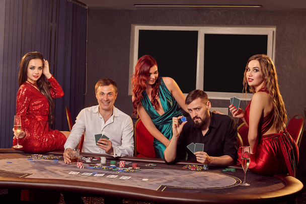 Eine Gruppe junger aufgeregter Freunde spielt an einem Pokertisch im Casino und blickt in die Kamera. Die Jugend geht Wetten ein und wartet auf einen großen Gewinn. Glücksspiel um Geld. Glücksspiele. - Foto, Bild