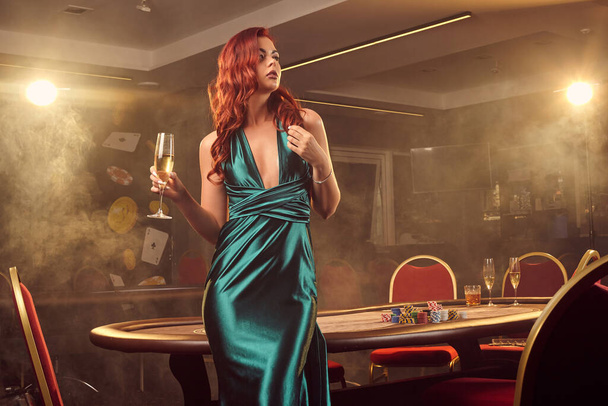 Νεαρή όμορφη γυναίκα ποζάρει ενάντια σε ένα τραπέζι πόκερ στο πολυτελές καζίνο. - Φωτογραφία, εικόνα