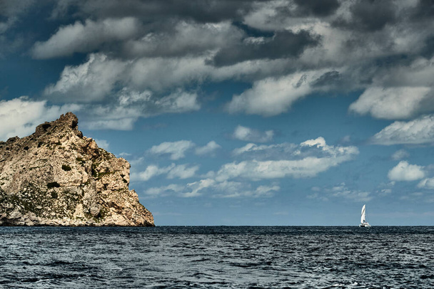 The Landscape of the balearic sea and improbable mountains, azure water, the storm sky, lonely buildings at tops of mountains, sail boat is on background - Foto, Bild