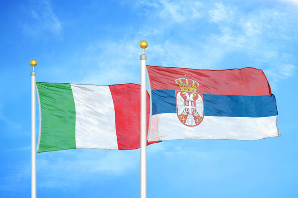 Italien und Serbien zwei Flaggen auf Fahnenmasten und blauer wolkenverhangener Himmel - Foto, Bild